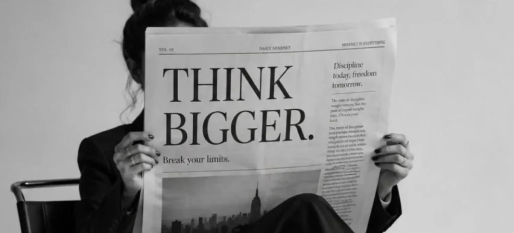 Moteris skaito laikraštį su antrašte „Think bigger“