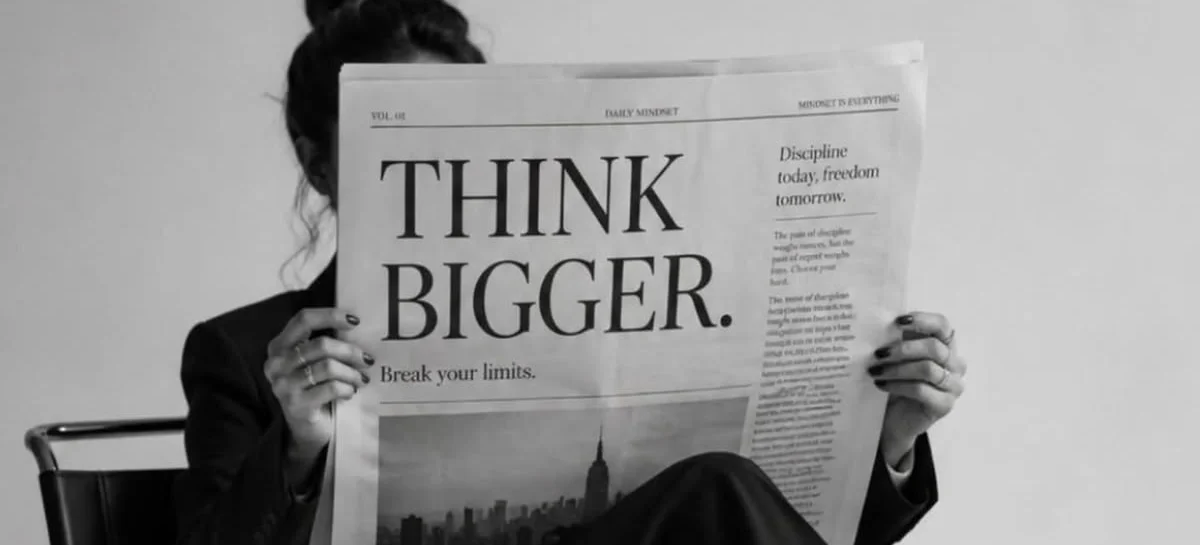Moteris skaito laikraštį su antrašte „Think bigger“